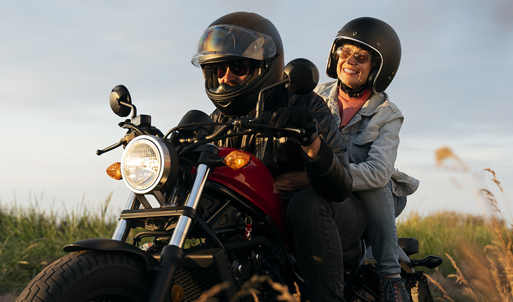 couple en moto avec des casques noirs à travers les champs